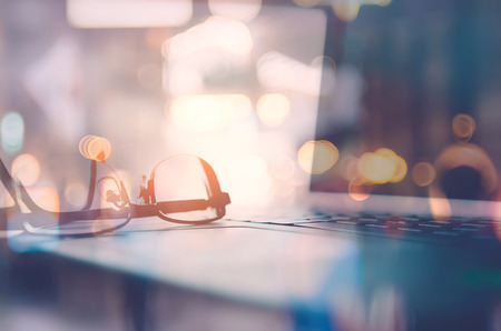 Business economic and technology working concept. Close up glasses on notebook with window light double expose with blur people bokeh light background. Vintage tone filter effect color style.の写真素材