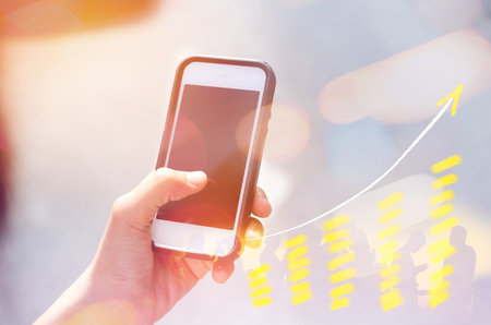 Business economic technology working concept. Woman using smart phone street double exposure graph money stock trading up trend arrow bar bokeh people background.Vintage tone filter effect color styleの写真素材