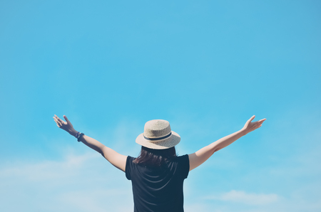 Freedom feel good and travel adventure concept. Copy space of silhouette woman rising hands on blue sky and white cloud with sun light background. Vintage tone filter effect color style.の写真素材