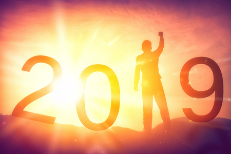 Happy new year and holiday concept. Man hand raising on top of mountain and number 2019 with sunset sky and cloud abstract background. Vintage tone filter effect color style.の写真素材