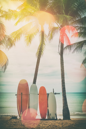 Surfboard and palm tree on beach double exposure with colorful bokeh sun light texture abstract background. Summer vacation and sport extreme concept. Vintage tone filter color style.の写真素材