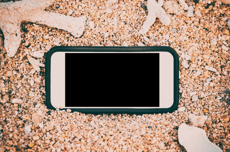 Smart phone on tropical sand beach with bokeh sun light wave texture background. Black copy space of technology and travel nature concept. Vintage tone filter effect color style.の写真素材