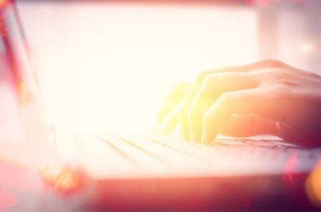 Woman hand using keyboard laptop on wood table in coffee shop double exposure with colorful bokeh light abstract background. Business technology and freelance concept. Vintage tone filter effect color style.の写真素材