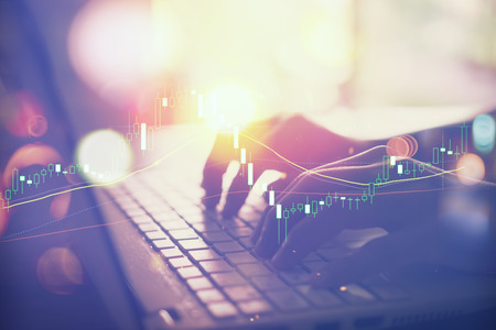 Business economic and technology working concept. Woman hand using keyboard notebook double exposure with graph money stock trading and blur bokeh light background. Vintage tone filter effect color style.の写真素材