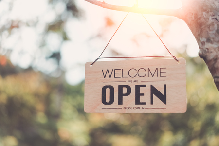Wooden open sign hanging on tree with green nature bokeh sunlight background. Business finance and service concept. Vintage tone filter effect color style.の写真素材