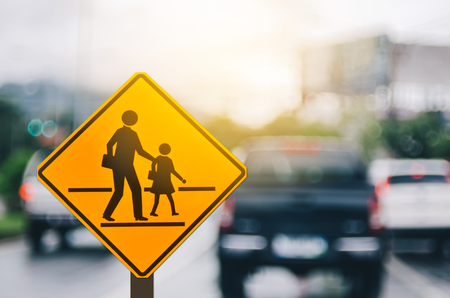 School zone warning sign on blur traffic road with colorful bokeh light abstract background. Copy space of transportation and travel concept. Vintage tone filter effect color style.の写真素材