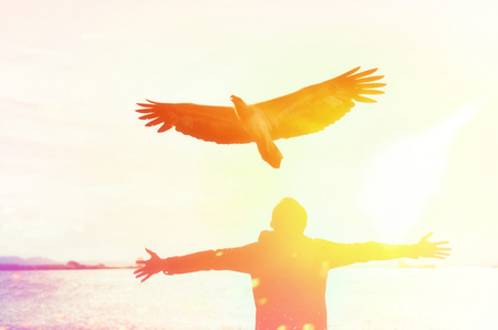 Man raise hand up at beach and sunset sky with eagle bird fly abstract background. Copy space freedom travel adventure and business victory concept. Vintage tone filter effect color style.の写真素材