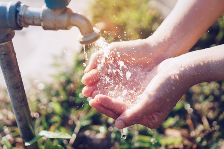 Water from tap to woman hand in nature green park sunset time and bokeh sun light abstract background. Environment and health care concept. Vintage tone filter effect color style.の写真素材