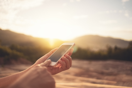 Woman hand using smart phone on top of mountain with sunset sky abstract background. Copy space technology business and travel nature holiday concept. Vintage tone filter effect color style.の写真素材