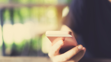 Woman hand using smart phone in cafe with green nature bokeh abstract background. Copy space of technology and business concept. Shallow depth of field. Vintage tone filter color style.の写真素材
