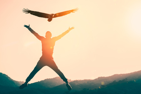 Man jumping on top of mountain and sunset sky with eagle bird fly abstract background. Copy space...