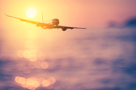 Airplane flying over blur tropical beach bokeh sun light wave and sunset sky abstract background. Copy space of business summer vacation and travel adventure concept. Vintage tone filter effect color.の写真素材