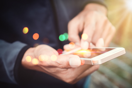 Close up man hand hold using smart phone on outdoor park street double exposure colorful bokeh abstract background. Copy space of technology business and travel holiday concept. Vintage tone filter effect color style.の写真素材