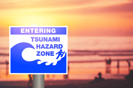 Tsunami warning sign on blur people relax on tropical sunset beach with bokeh sun light wave abstract background. Copy space of summer vacation and business travel concept. Vintage tone color style.の写真素材