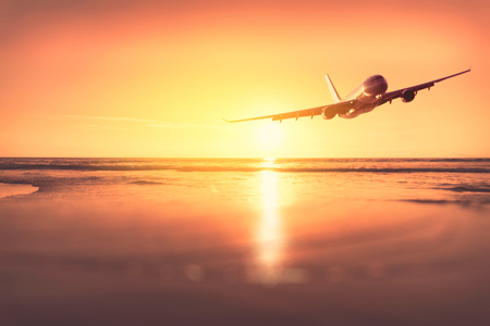 Airplane flying over blur tropical beach bokeh sun light wave and sunset sky abstract background. Copy space of business summer vacation and travel adventure concept. Vintage tone filter effect color.の写真素材