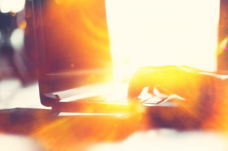 Woman hand using keyboard laptop on wood table in coffee shop double exposure with colorful bokeh light abstract background. Business technology and freelance concept. Vintage tone filter effect color style.の写真素材