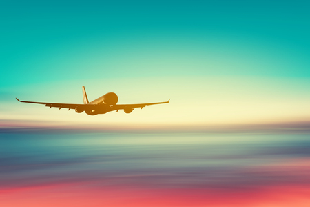 Airplane flying over blur tropical beach with smooth wave and sunset sky abstract background. Copy space of business summer vacation and travel adventure concept. Vintage tone filter effect color.の写真素材