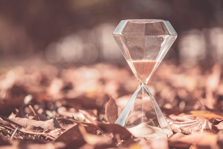 Hourglass on dry leaves with bokeh sun light abstract background. Copy space of time and life...