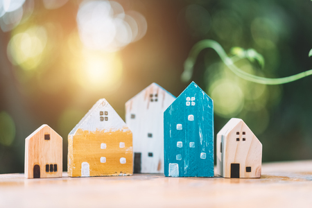 Small model houses on wooden table with nature green bokeh sunlight abstract background. Copy space of business finance and life family concept. Vintage tone filter effect color style.の写真素材