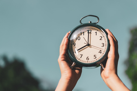 Woman raise hand up and holding clock on blue sky abstract background. Copy space of time and lifestyle concept. Vintage tone filter effect color style.の写真素材