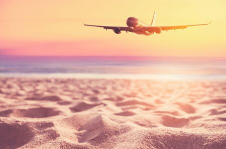 Airplane flying over blur tropical beach and sunset sky abstract background. Copy space of business summer vacation and travel adventure concept. Vintage tone filter effect color style.の写真素材