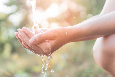 Water from tap to woman hand in nature green park sunset time and bokeh sun light abstract background. Environment and health care concept. Vintage tone filter effect color style.の写真素材