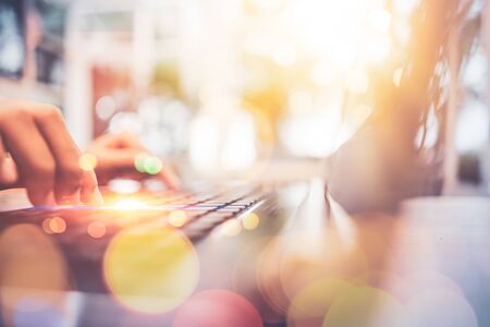Woman hand using keyboard laptop on wood table in coffee shop double exposure with colorful bokeh...