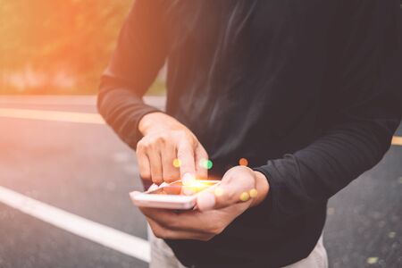 Close up man hand hold using smart phone on outdoor park street background. Copy space of technology...