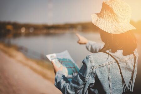 Woman looking map for travel at lake background with sunset sky. Copy space of travel adventure and...