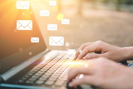 Woman hand using keyboard laptop in outdoor nature park background with email icon flying abstract....