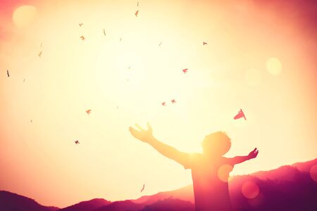 Freedom feel good and travel adventure concept. Copy space of silhouette man rising hands on sunset sky double exposure colorful bokeh and bird fly background. Vintage tone filter effect color style.の写真素材