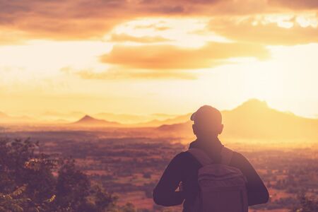 Copy space of backpack man looking view on top of mountain and sunset sky abstract background. Freedom travel adventure and business victory concept. Vintage tone filter effect color style.の写真素材