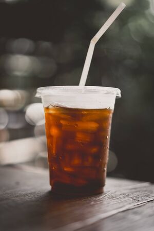 Ice coffee on wood table in cafe with green bokeh light abstract background. Vintage tone filter color style.の写真素材