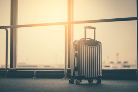 Travel bag in airport terminal gate with window sunset light background. Travel adventure and vacation freedom concept. Vintage tone filter effect color style.の写真素材