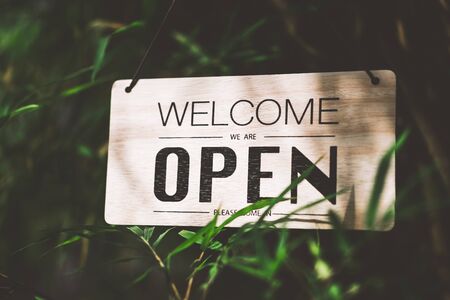 Wooden open sign hanging on bamboo tree with green nature bokeh sunlight background. Business...