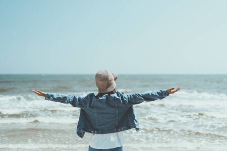Freedom feel good and travel adventure concept. Copy space of woman raise hands with blue sky and wind wave on beach background. Vintage tone filter effect color style.の写真素材