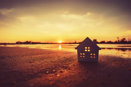 Small home model on sunset beach sand texture background. Copy space of family lifestyle and business real estate concept. Vintage tone filter effect color style.の写真素材
