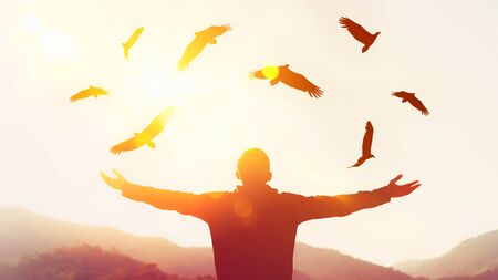 Man raise hand up on top of mountain and sunset sky with eagle birds fly abstract background. Copy space freedom travel adventure and business victory concept. Vintage tone filter effect color style.の写真素材