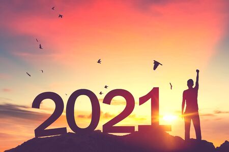 Man raise hand up on sunset sky with birds flying at top of mountain and number like 2021 abstract background. Happy new year and holiday concept. Vintage tone filter effect color style.の写真素材