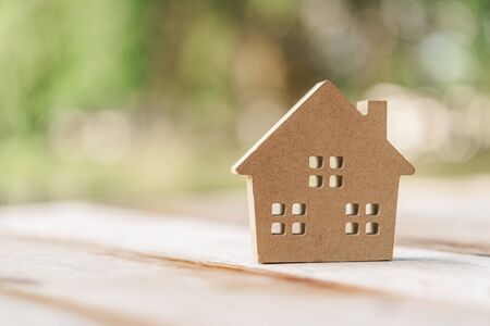 Small home model on wooden table with nature green bokeh abstract background. Family life and business real estate concept. Vintage tone filter effect color style.