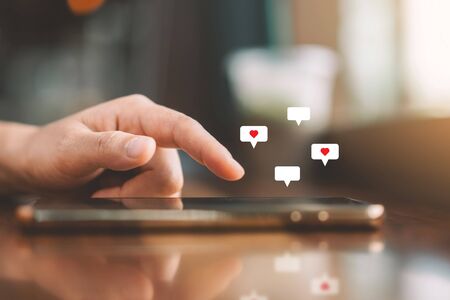 Woman hand using smartphone with heart icon at coffee shop background. Technology business and...