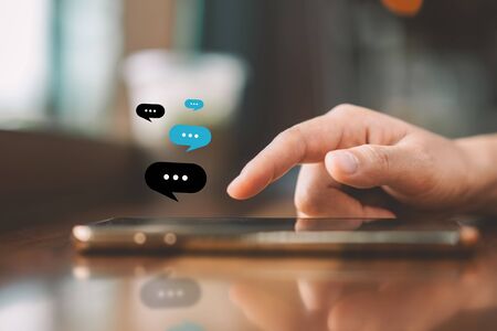 Woman hand using smart phone with chat icon graphic at coffee shop abstract background. Technology business and freelance concept. Vintage tone filter effect color style.の写真素材