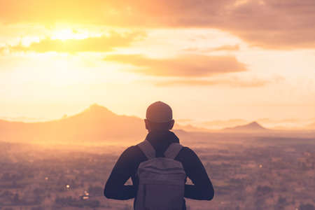 Backpacker man standing at top of mountain looking view landscape with sunset sky white cloud abstract background. Copy space travel adventure holiday and freedom feel good concept. Vintage tone color.の写真素材