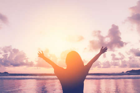 Happy woman raise hand up at tropical beach with sunset sky background. Travel vacation and freedom...