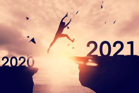 Silhouette man jumping between cliff with number 2020 to 2021 at tropical sunset beach. Freedom challenge and travel adventure holiday concept. Vintage tone filter effect color style.の写真素材