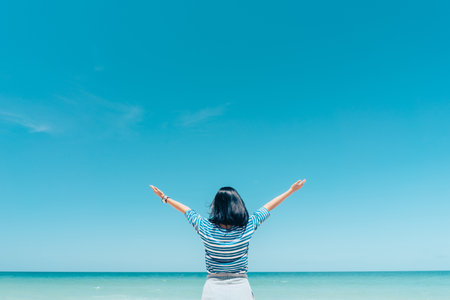 Happy woman raises her hand up at a tropical beach with blue skyの写真素材