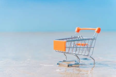 Shopping basket cart on sand beach with blue sky background. Summer sale and business service concept. Vintage tone filter effect color style.の写真素材
