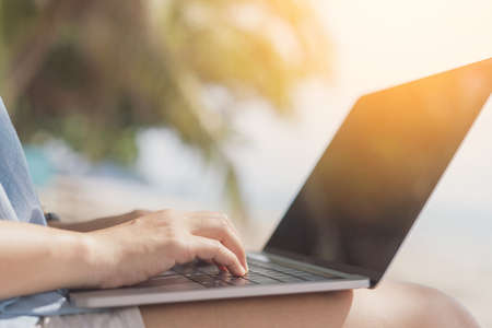 Woman using laptop on tropical beach background. Freelance working and travel vacation concept.の写真素材