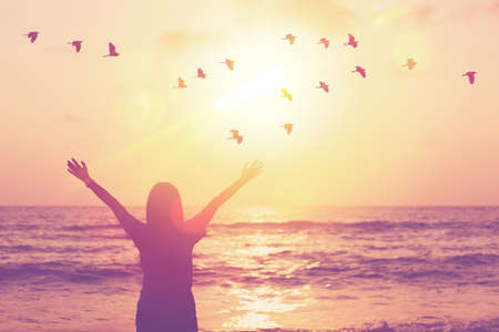 Copy space of woman raise hand up on sunset sky at beach and island double exposure birds fly colorful bokeh abstract background. Freedom and travel adventure concept. Vintage tone filter color style.の写真素材