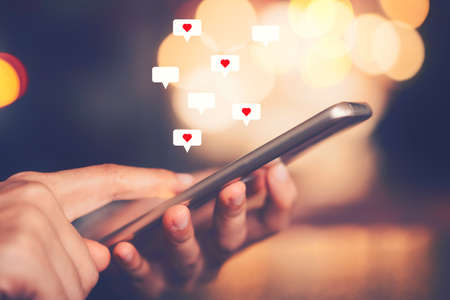 Woman hand using smartphone with heart icon at coffee shop background. Technology business and...